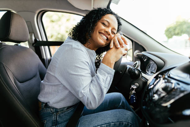 young and cheerful woman enjoying new car hugging steering wheel sitting inside. woman driving a new car. - rijden activiteit stockfoto's en -beelden