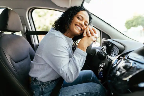 Photo of Young and cheerful woman enjoying new car hugging steering wheel sitting inside. Woman driving a new car.