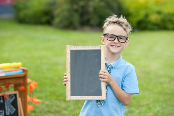 a schoolboy holding a chalk board sitting on books. Kid holding a black board. Empty space for text. School lessons. Back to school.