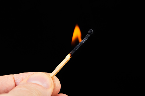 A man holds a burning match in his hand on a dark background