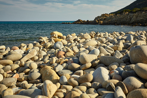 Detail of some white pebbles on a typical beach of the southern coast of southern Sardinia in Italy, with the background of the rest of the beach and the sea.