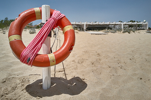 Symbolic image of a life buoy with rope hanging on a pole in the beach.