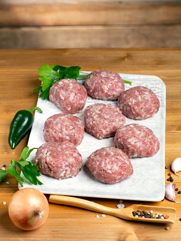 Turkey raw meatballs with vegetables on plate on wooden background.