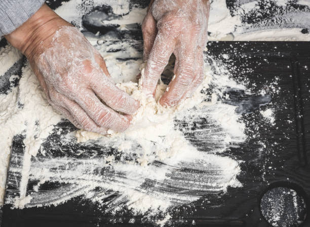 istock two female hands knead the dough from white wheat flour on a black table, top view 1417077560