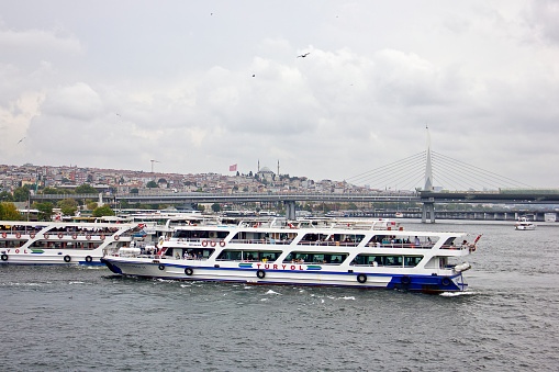 Istanbul,Turkey - August 10, 2022: Golden horn view from Galata bridge that linked eminönü and karaköy, there are lots of people on the bridge, lots of them are fishing, and beyond the bridge you see the süleymaniye mosque and fire tower in a cloudy summer day.