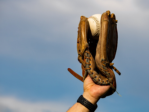 A close-up of a used dirty white softball in a leather glove sitting in the grass