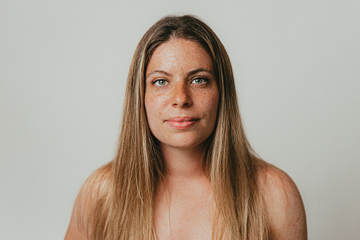 Portrait of a beautiful young freckled woman with healthy and clear skin, studio shoot in front of white background