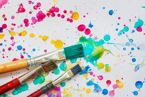 Artistic paint brushes on background of painted paper with bright spots and splashes, art concept