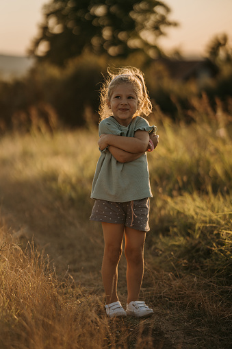 Cute little girl standing on a meadow in nature, she is hugging herself.