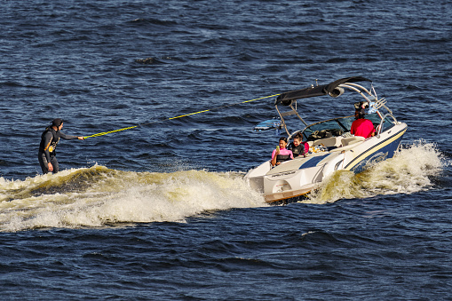 Russia, St. Petersburg, 29 July 2022: Man riding wakeboard on wave of motorboat in summer river, wakesurfing on river summertime leisure. High quality photo