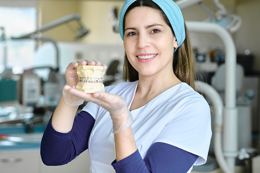 Dentist looking at the camera and smiling holding a dental prosthesis with brackets