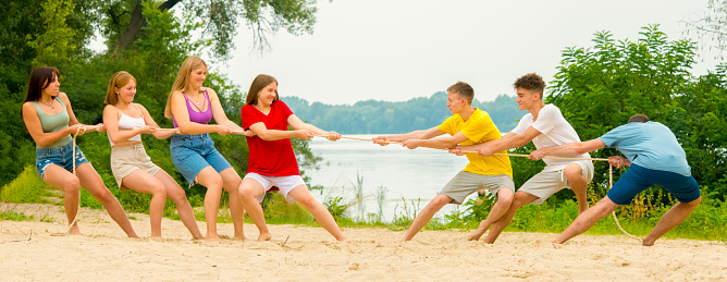 a team of teenagers tug of war on the shore. a group of boys and girls compete in tug of war.