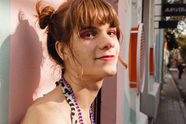 portrait of a smiling young transgender woman leaning against a wall in the street stock photo