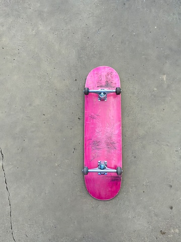 Scrached up pink skateboard laying on smooth concrete surface at local skatepark - black griptape