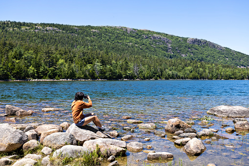 Teen takes in the gorgeous scenery at Jordan Pond in Acadia National Park, Maine. The pond covers 187 acres with a shoreline of 3.6 miles. The clear water of the pond provides drinking water for the residents in the surrounding area.