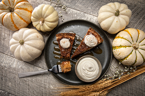 This is a close up photo of white pumpkins with Baby's Breath flowers on a wood table background with Cheesecake Pumpkin Pie and cinnamon whip cream. There is space for copy. This is a nice high key image that would work well for autumn, Thanksgiving and a holiday Halloween season in the fall.