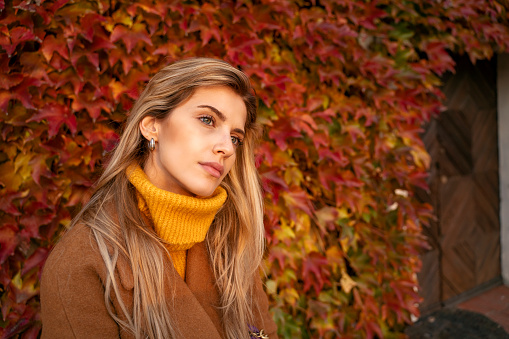 Pensive sad, blonde girl posing in colorful leaves in autumn, seasonal depression