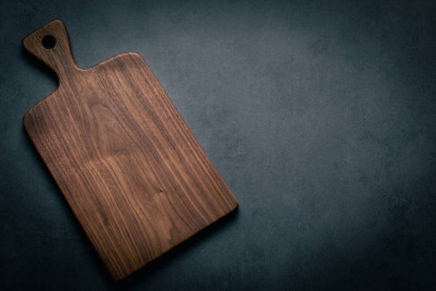 A handcrafted black walnut wood chopping board sits on a dark-toned tabletop. walnut wood board.
