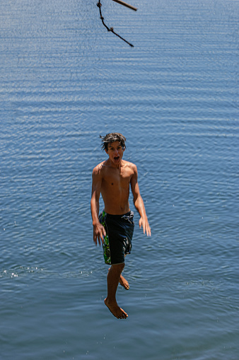 Teenage Latino boy having water fun on rope swing.\n\nTaken at Bear Lake, Bear Valley, California, USA
