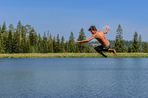 Teenage Latino boy having water fun on rope swing.\n\nTaken at Bear Lake, Bear Valley, California, USA
