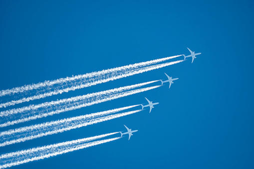 Many distant passenger jet planes flying on high altitude on clear blue sky leaving white smoke trace of contrail behind. Busy air transportation concept.