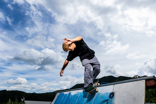 A young male Japanese rider practicing tricks on a half pipe on his skateboard.