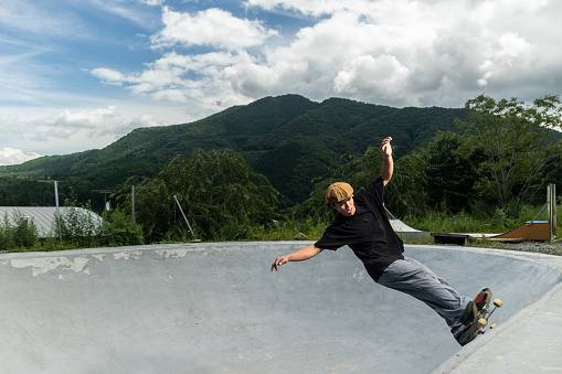 A young male Japanese rider performs tricks on his skateboard in a concrete bowl.