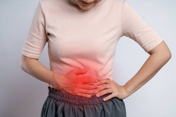 Asian woman was sick with stomach ache putting her hands on belly with red spot. Asian woman was sick with stomach ache, putting her hands on belly with red spot, standing isolated on white background. gastroenteritis stock pictures, royalty-free photos & images