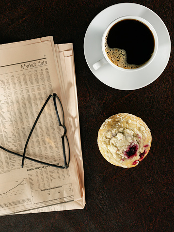 Looking down on a coffee cup, muffin and newspaper on desktop