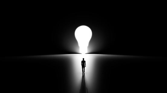 3D Silhouette of a Man Walking to Reach His Ideas, Lightbulb Shaped Hole in the Wall Shinning Light Towards Him, Black Background.