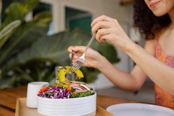 Woman using smartphone while having plant-based brunch. Smiling Asian woman using smart phone chatting with friends while eating tofu salad a in backyard. image based social media photos stock pictures, royalty-free photos & images