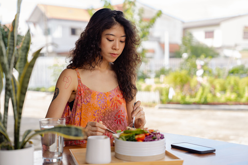 Healthy Asian woman eating healthy vegan plant-based salad while relaxing at home.