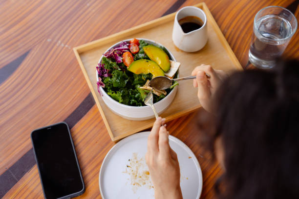 Woman using smartphone while having plant-based brunch. Smiling Asian woman using smart phone chatting with friends while eating tofu salad a in backyard. image based social media photos stock pictures, royalty-free photos & images