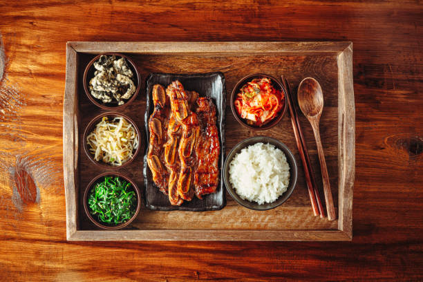 Famous Korean dish Beef Galbi BBQ with white rice, kimchi, spinach, and some side dishes nicely placed on a wooden tray.