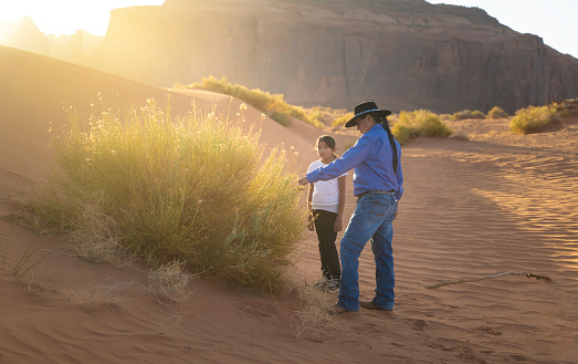 Father showing a native plant to her daughter in Monument Valley at sunset