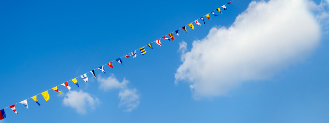 Garland of small flags of different countries against the background of a blue sky with clouds. Festive tape, party, fair, festival decorations. Banner, space for text