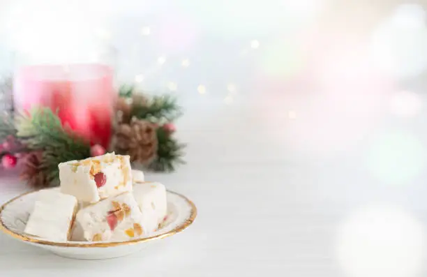 Nougat on Plate with Christmas Candle and Lights on Light Background with Copy Space Horizontal