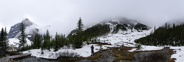 A mid adult woman hikes along a mountain path covered in snow high in the mountains in the Banff National Park. Things to do around Lake Louis.