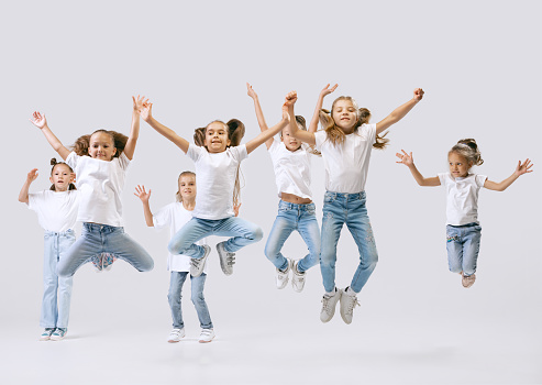 Joy, fun and happiness. Portrait of happy, active little girls, sportive kids in casual clothes dancing isolated on white studio background. Concept of music, fashion, art, childhood, hobby.