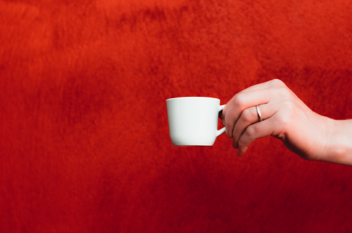 Female arm holding a coffee cup against a red background. Not a composite.