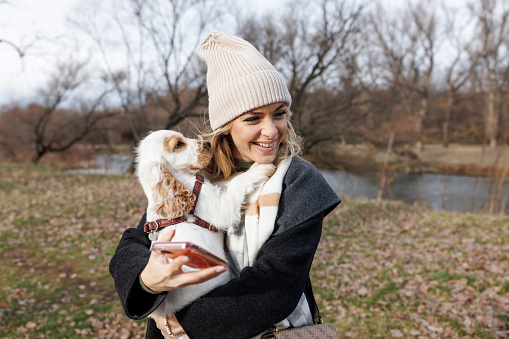 Beautiful young woman holding her new puppy and standing in nature by the river on autumn day