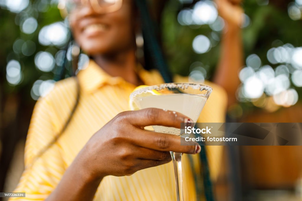 Close up shot of cheerful young woman enjoying a margarita cocktail Low angle view of cheerful young woman holding and enjoying a martini glass with margarita cocktail during a relaxing summer garden party. Part of a series. Cocktail Stock Photo