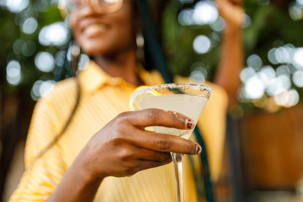 Close up shot of cheerful young woman enjoying a margarita cocktail Low angle view of cheerful young woman holding and enjoying a martini glass with margarita cocktail during a relaxing summer garden party. Part of a series. alcohol drink stock pictures, royalty-free photos & images