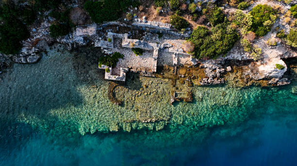 Simena - flooded ancient Lycian city Kekova island Ruins of antique architecture, aerial view of submerged historic sunken city, location to explore undersea, clean undersea, discovery spot for divers Aerial view of Sunken city in Kekova, Antalya. 

After the Italian occupation of Kastelorizo, Kekova — which at that time was temporarily inhabited during summer because of wood harvest — was disputed between Italy and Turkey. The 1932 Convention between Italy and Turkey assigned it to Turkey.

On its northern side there are the partly sunken ruins of Dolchiste/Dolikisthe, an ancient town which was destroyed by an earthquake during the 2nd century. Rebuilt and still flourishing during the Byzantine Empire period, it was finally abandoned because of Arab incursions. Tersane (meaning "dockyard", as its bay was the site of an ancient city Xera and dockyard, with the ruins of a Byzantine church) is at the northwest of the island.

The Kekova region was declared a specially protected area on 18 January 1990 by Turkish Ministry of Environment and Forest. All kinds of diving and swimming were prohibited and subject to special permits from governmental offices. In later years the prohibition has been lifted except for the part where the sunken city is. kekova stock pictures, royalty-free photos & images