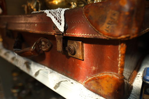 A brown vintage suitcase with metal locking mechanisms in dappled sunlight.