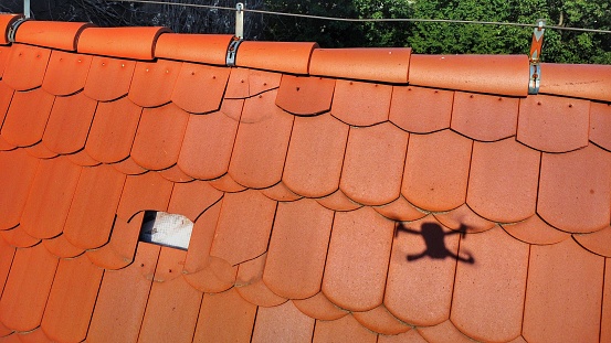 Inspection of a red, damaged ceramic tile roof. Visible shadow of a flying drone