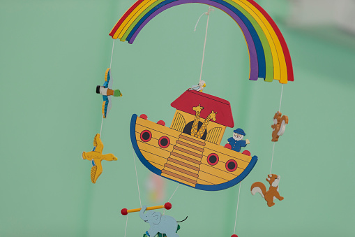 Colorful toy hanging over the crib on green background. Rainbow, ship, animals.