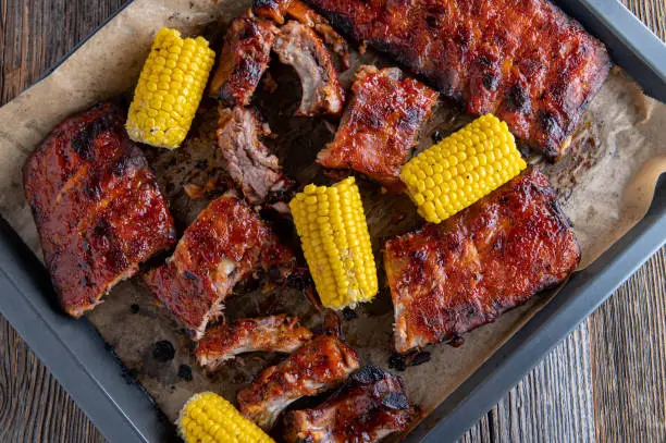 Oven baked and marinated pork ribs with corn on the cop on a baking tray.
