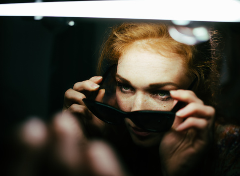 A young woman takes another serious look in the mirror before putting on a pair of dark sunglasses.