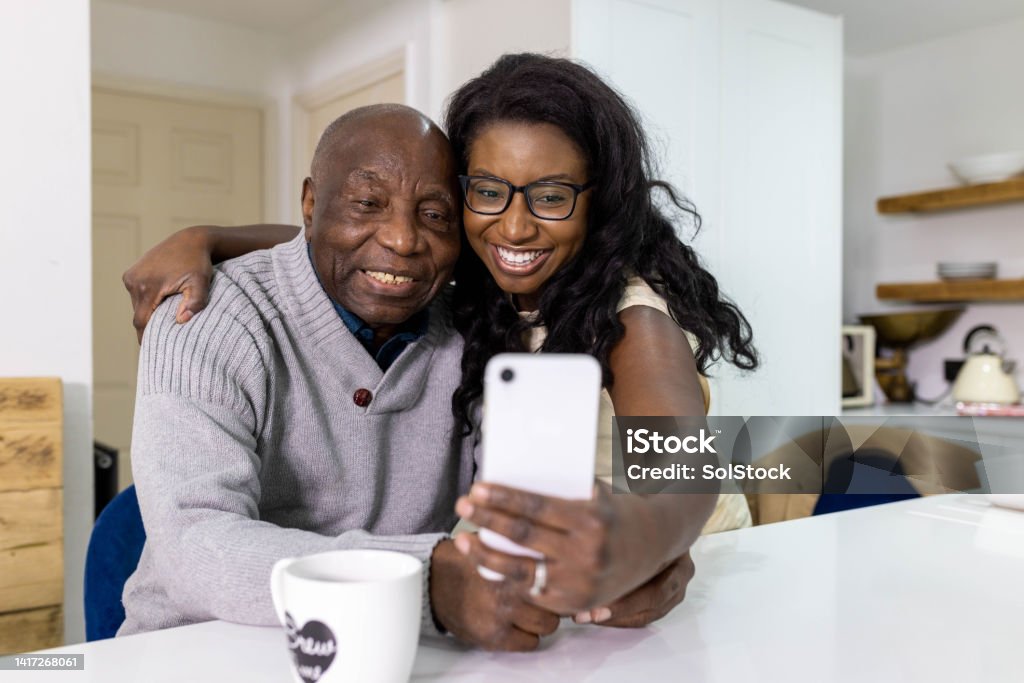 Lets Take A Selfie Dad Front view mid adult woman takes a selfie with her father who is sitting down at the kitchen island. They are both smiling and looking into the camera. 35-39 Years Stock Photo